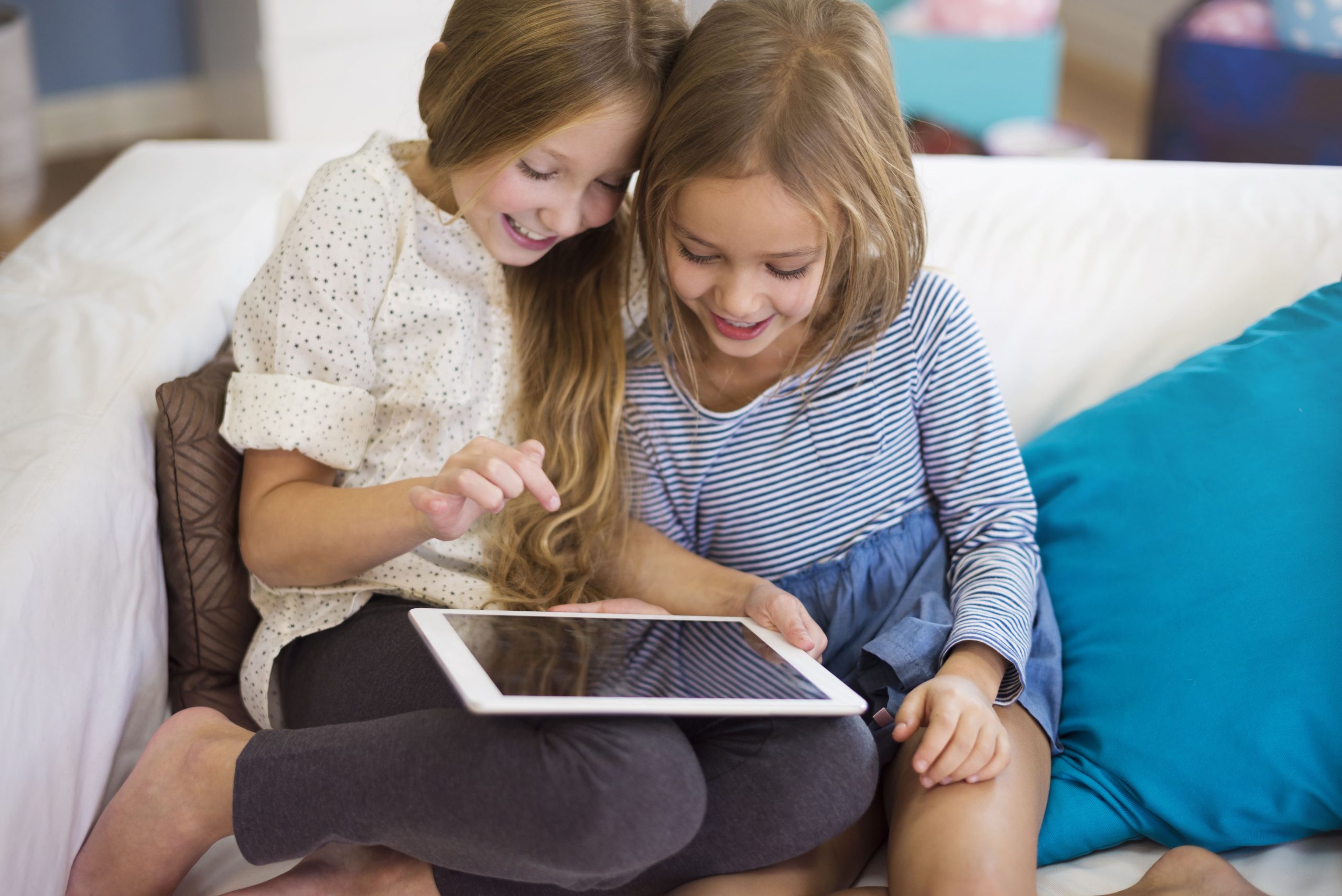 Mergaitės sėdi ant sofos ir žiūri iPad