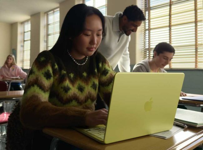 MacBook Neo. Mergina su citrininės spalvos laptopu.