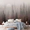 Artgeist Fototapetas - Bird's flight over treetops - landscape of a dark forest in fog