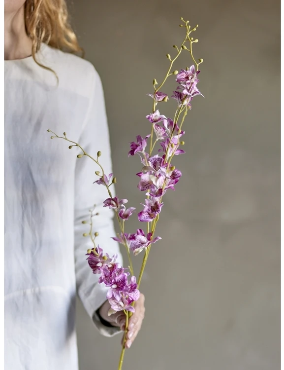 Rožinė dirbtinė orchidėja stiebe, laikoma rankoje