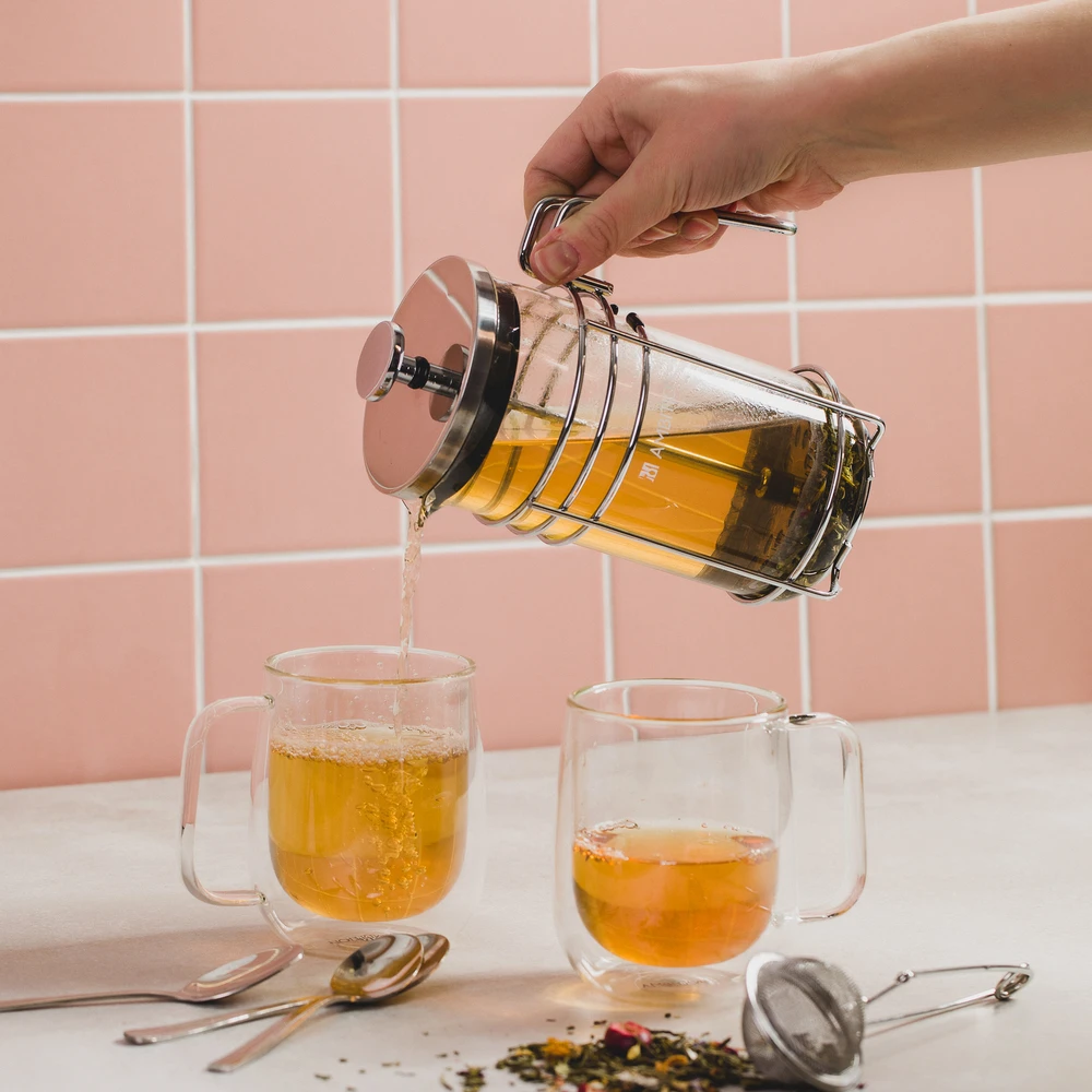 Stiklinis french press indas su metaliniu rėmeliu pilant arbatą
