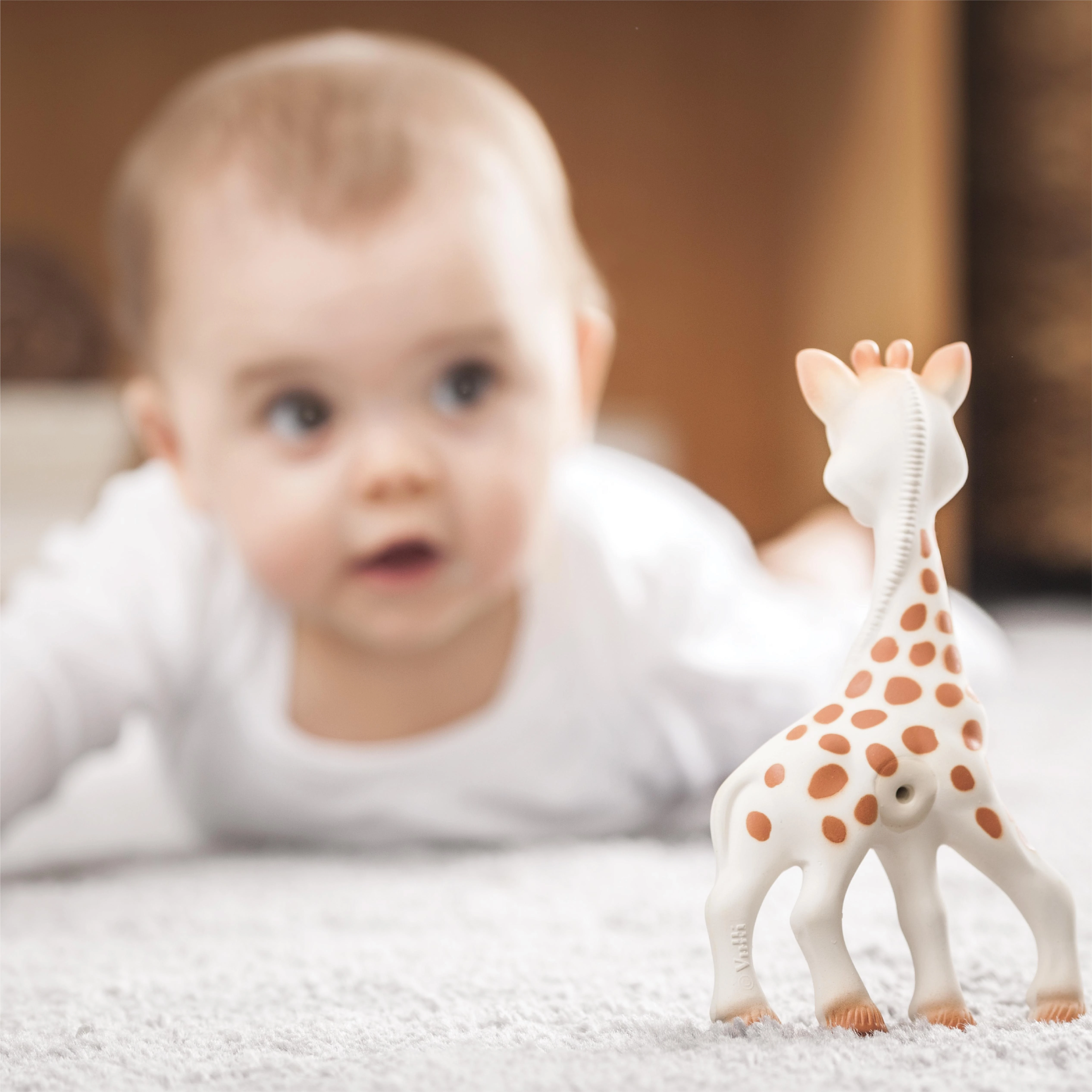Sophie la girafe kramtukas žaidžiančio kūdikio fone